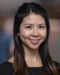 Woman with medium length dark brown hair smiles in black shirt against dark background
