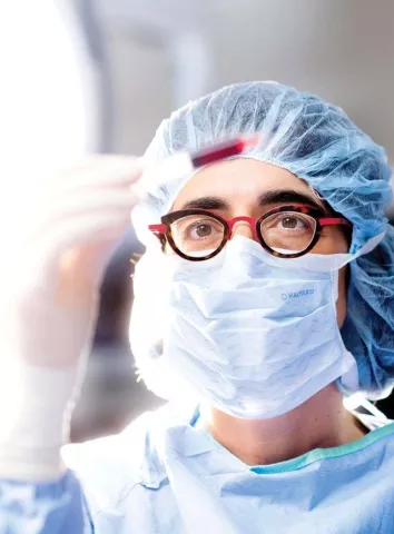 Tippi MacKenzie in surgical scrubs looking at a syringe of stem cell blood