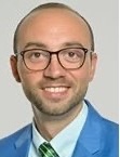 Akos Herzeg, MD, PhD, UCSF, smiling in bright blue blazer with white dress shirt and tie on grey background