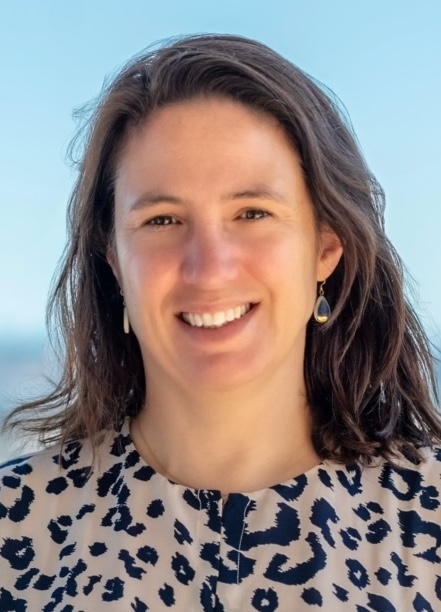 Billie Lianoglou, MS, LCGC, UCSF smiling in blue top and necklace with outdoor setting