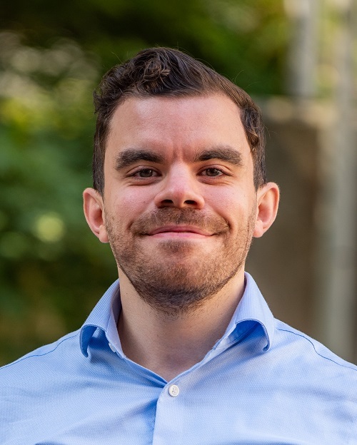 Beltran Borges, MD, research fellow UCSF, smiling in plaid dress shirt short brown hair and outdoor backdrop