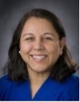 Deeksha Bali, PhD, Duke University, smiling with short brown hair and dark background