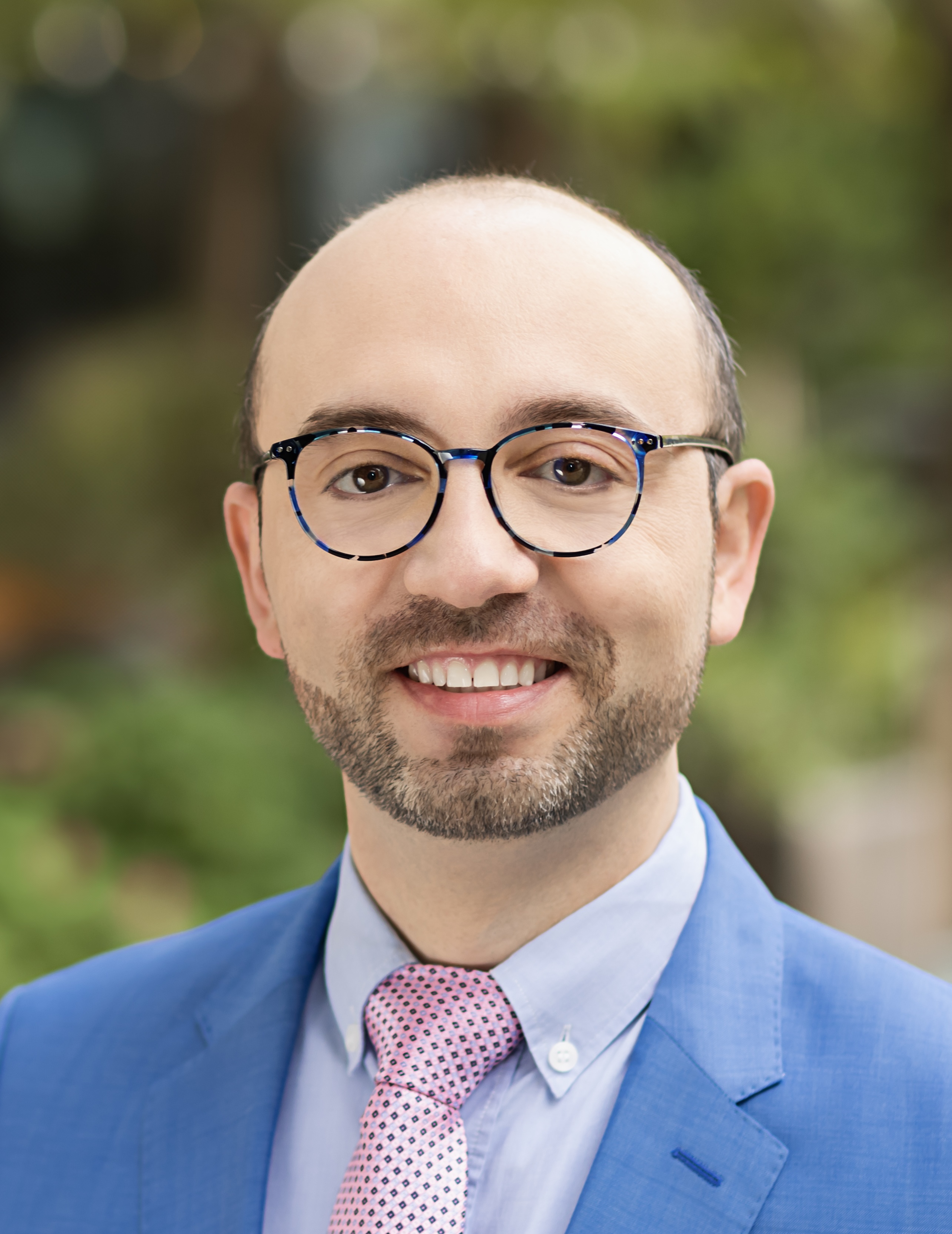 Akos Herzeg, MD, PhD, UCSF, smiling in bright blue blazer with white dress shirt and tie on grey background