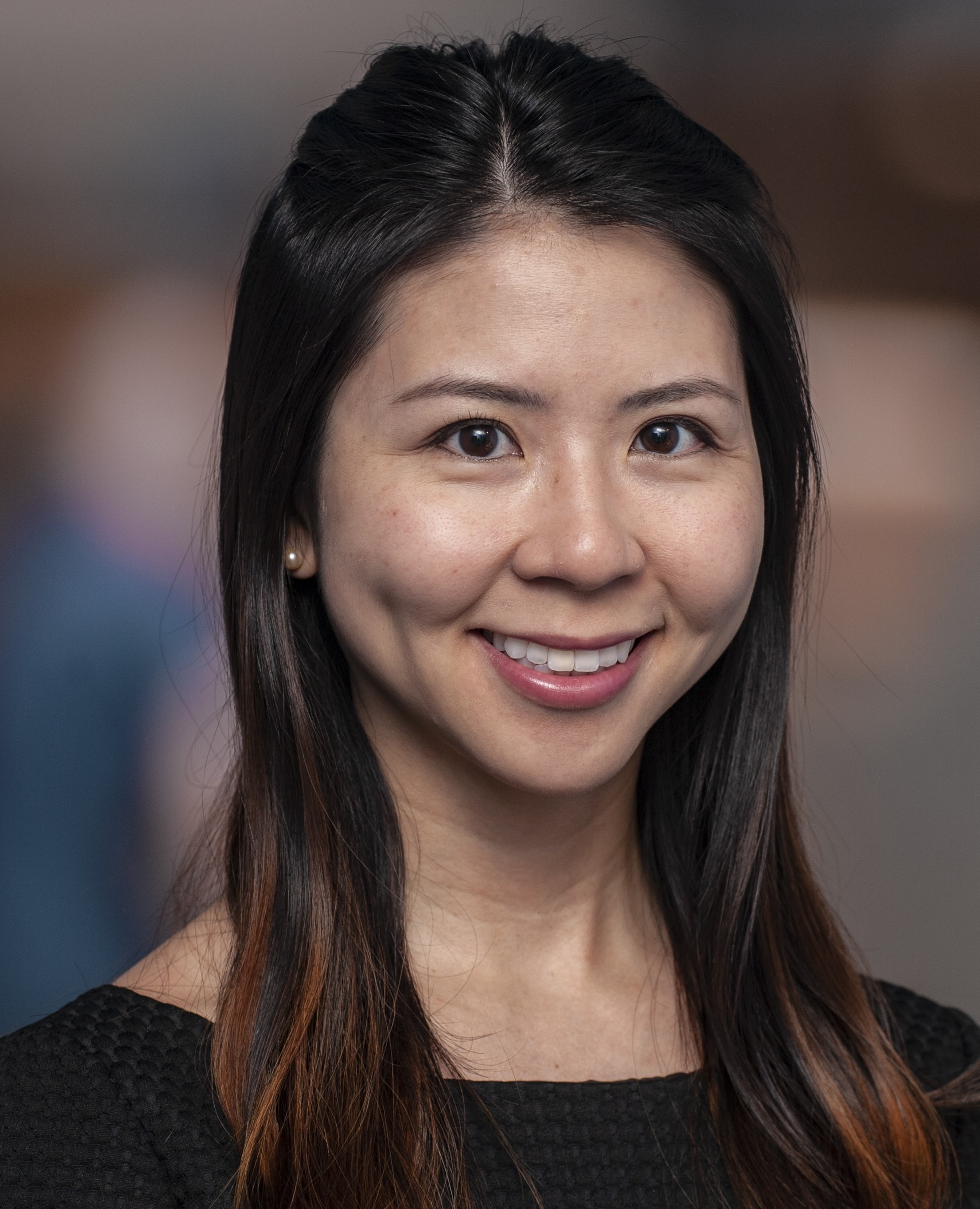 Woman with medium length dark brown hair smiles in black shirt against dark background