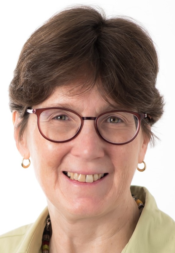 Renata Gallagher, MD, PhD, UCSF Emeritus, smiling in green dress shirt with short length hair and light grey backdrop